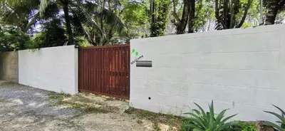a white fence with a red gate and trees at Bassara House 2 bedroom in Koh Lone