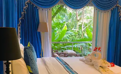 a bedroom with a bed with blue curtains and a window at BOUTIQUE-VILLA with Suites & Rooms in Karon Beach