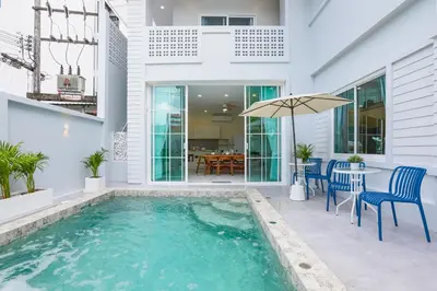 a swimming pool in a house with chairs and an umbrella at Seven Heaven Patong Villa in Patong Beach