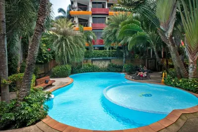 a large swimming pool with palm trees in front of a building at Stunning 60 sqm Studio at NaiHarn Beach Condo, Walk to Beach, Your Tropical Retreat! in Rawai Beach