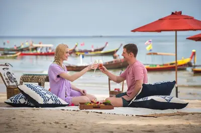 a man and woman sitting on the beach drinking wine at Keemala - Tent Pool Villa in Kamala Beach
