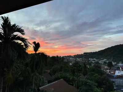 a sunset over a city with a palm tree at Kata Sea Cloud Villa\u534a\u5c71\u6d77\u666f\u72ec\u680b\u522b\u5885 in Kata Beach