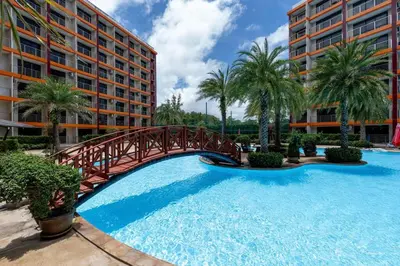 a bridge over a swimming pool with palm trees and buildings at 1 BR apartment 777 Beach Condotel in Mai Khao Beach
