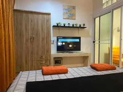 a room with a tv and a bed with orange pillows at Bestin Karon 1 - Apartment GF- 1 min from Karon beach in Karon Beach