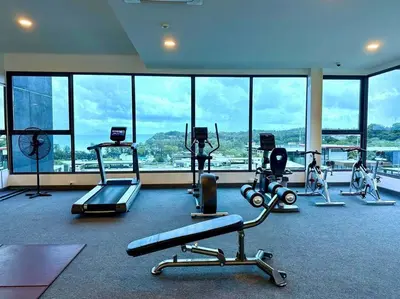 a gym with cardio equipment in a large room with windows at One bedroom apartment Calypso Garden in Phuket Town