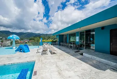 a blue building with a swimming pool with a playground at Deluxe Twin Bed Apartment by Renttini in Kamala Beach