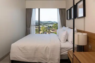 a bedroom with a white bed with a large window at Laguna Lakeside Apartment Phuket Bang Tao in Bang Tao Beach