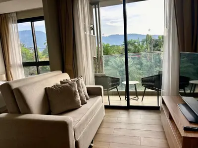 a living room with a couch and a large window at Cozy apartment with a Resort Facilities in Bangtao in Bang Tao Beach