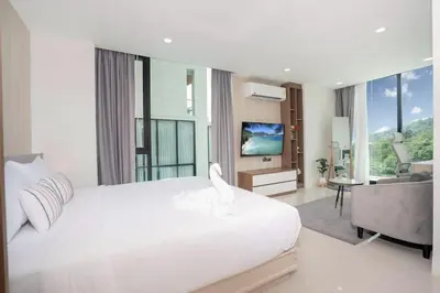 a bedroom with a white bed and a living room at Beach, Relax & Fun! VV Patong 2BR Apartment C201 just 5 min drive from Patong Nightlife in Patong Beach