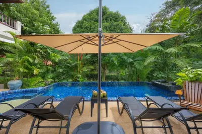 a patio with chairs and an umbrella next to a pool at Meraya Villa with Private Pool Near Nai Harn Beach in Rawai Beach