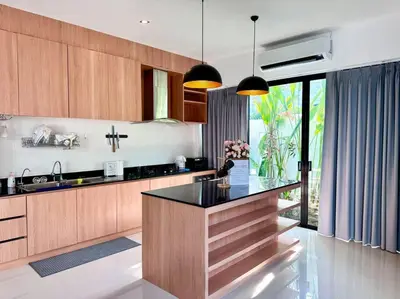 a kitchen with wooden cabinets and a black counter top at Funtime pool villa in Kata Beach