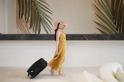a woman in a yellow dress with a hat and a suitcase at Lalynn Resort & Villas, Phuket in Thalang