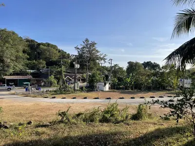 a parking lot with a road and trees in the background at Green Gen Hotel, Mueang Phuket in Phuket Town