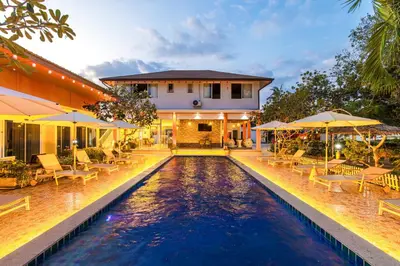 a pool with chairs and umbrellas in front of a house at Tongtong Garden Holiday Hotel\u666e\u5409\u5c9b\u901a\u901a\u82b1\u56ed\u9152\u5e97 in Rawai Beach
