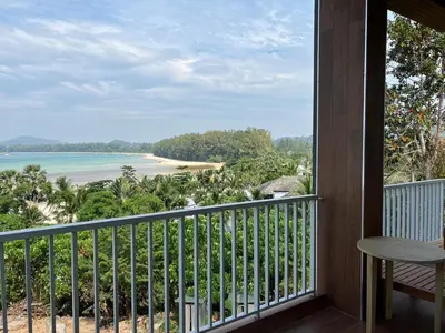 a room with a balcony with a view of a beach at Beachfront Bliss at Naiyang Phuket by ALPHATEL in Phuket
