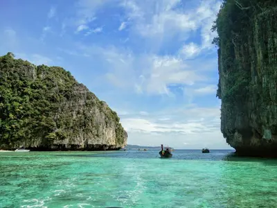 a boat in the water next to a rocky island at Summer Sea Phi Phi Island in Phi Phi Don