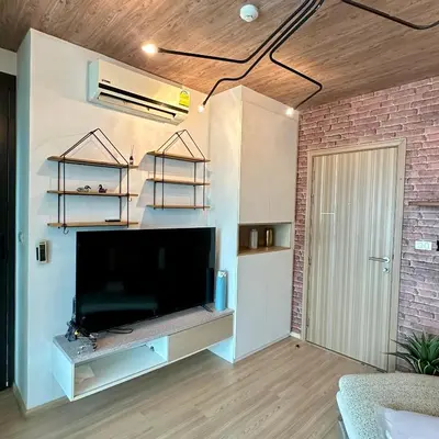 a living room with a large television and a brick wall at Connext Condominium By January in Ban Tha Khreng