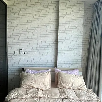 a bedroom with a white brick wall and a bed with pillows at Connext Condominium By January in Ban Tha Khreng