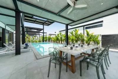 a dining table and chairs on a patio with a pool at New & Modern, Loft Style 4BR Villa Sunset Garden 3, 12m Salt Pool, just 10min drive Naiharn Beach in Rawai Beach