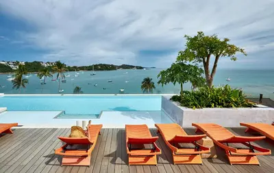 a pool with orange chairs and a view of the ocean at Bandara Beach Resort, Phuket in Panwa Beach
