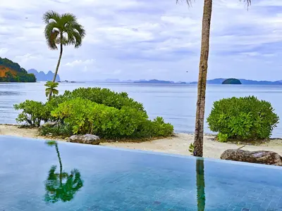 a swimming pool next to a beach with a palm tree at Luxury Beachfront BRAHMA Villa 4 Br at Ta-Ke Residence B in Phuket
