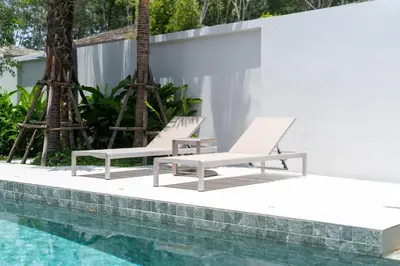 a pair of white lounge chairs next to a swimming pool at Bang Tao Botanica Modern Loft 3 bd in Ban Pak Lak