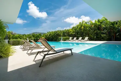 a row of lounge chairs next to a swimming pool at Luxurious 5BR Villa Mayacol with 17m Long Pool, NaiHarn in Rawai Beach