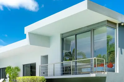 a white house with large glass windows at Luxurious 5BR Villa Mayacol with 17m Long Pool, NaiHarn in Rawai Beach
