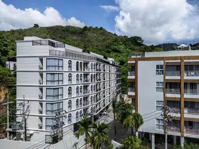 a white building with palm trees in front of a mountain at Palmetto Park Residence in Karon Beach