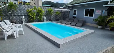 a swimming pool with two white chairs and a house at Karon Homes in Karon Beach