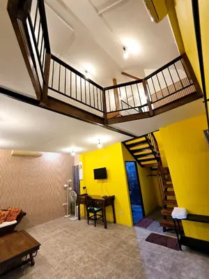 a living room with yellow walls and a table and stairs at Baibon3 Homestay Thalang Phuket in Ban Na Nai