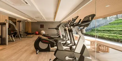a gym with treadmills and ellipticals next to a window at Baan Mai Khao Condo Phuket for rent in Phuket