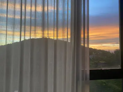 a view of a sunset from a window with a curtain at Patong Sea View pool view condo in Patong Beach