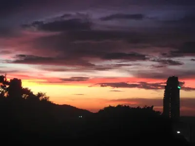 a sunset with a building and trees in the foreground at Ocean and Mountainviews, 2 Balconies in Patong Beach