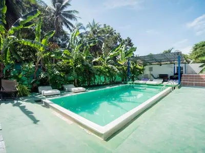 a swimming pool in a yard with chairs and trees at Los Patios Hostel Phuket in Mai Khao Beach