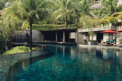 a swimming pool with blue water and palm trees at Keemala in Kamala Beach