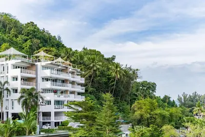 a white apartment building on a hill with trees at Large condo Surin-Bangtao Beach in Surin Beach