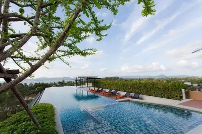 an infinity pool with chairs and a view of the mountains at Condo Surin-Bangtao Beach in Surin Beach