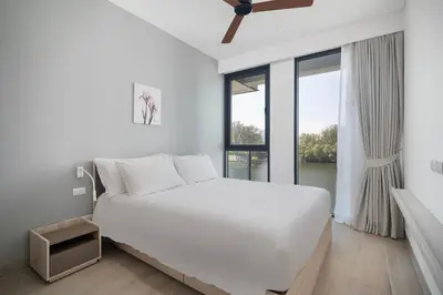a white bedroom with a large bed and a window at Cassia Residences in Laguna by Banyan Living in Laguna Phuket