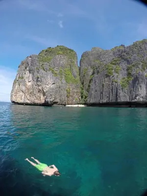 a person floating in the water near a rocky island at Babyshark Hostel - Loh Dalum Bay in Phi Phi Don