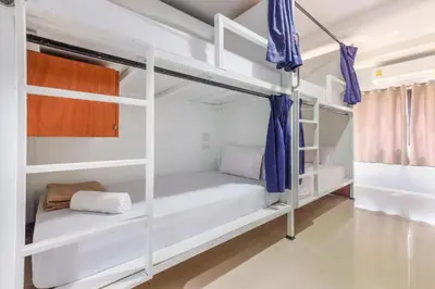 a room with white bunk beds with blue curtains at The Little Nest Phuket in Phuket Town