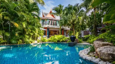 a swimming pool in front of a house with palm trees at Villa in the Park, Surin Beach, Phuket in Surin Beach