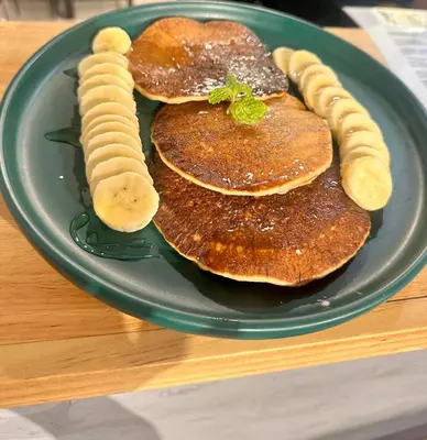 a green plate with pancakes and bananas on a table at Pupa Women Hostel in Patong Beach
