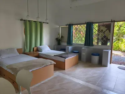 a room with two beds and a chair and windows at Niyang Siam House in Nai Yang Beach