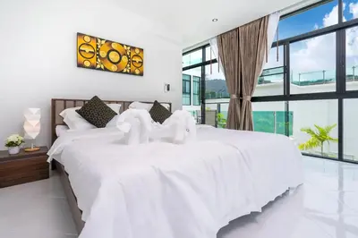 a white bedroom with a large white bed and large windows at Namara The Residences A in Kamala Beach