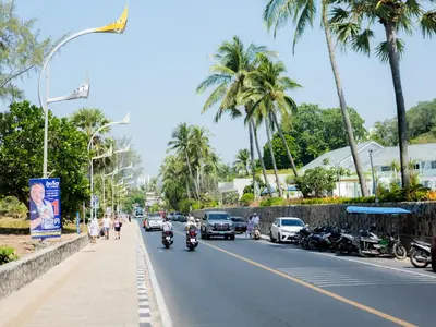 a street with cars and motorcycles on a road with palm trees at I Talay phuket in Karon Beach