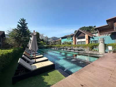 a pool with lounge chairs and an umbrella next to a house at โรงแรมชาวเกาะพีพี Chaokoh Phi Phi Island in Phi Phi Don