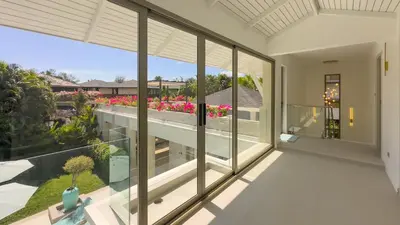 an open balcony with large glass windows and pink flowers at Beachfront Luxury villa near Banyan Tree in Layan Beach