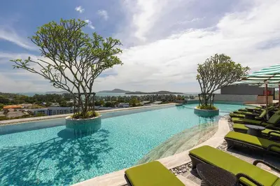 a large swimming pool with green chairs and trees at Condo with Roof top sea view in Rawai Beach