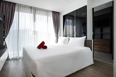 a red teddy bear sitting on top of a white bed at Elegant Natural Stay at VV Patong Apartment A401 in Patong Beach